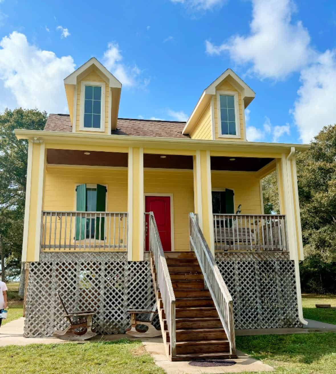 Exterior Painting Yellow house with front porch, red door, and two dormer windows under blue sky.